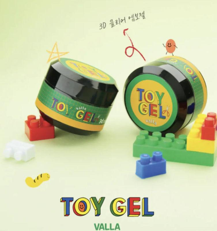 The image shows a Shopify product called "VALLA Toy Gel", which is a 3D clear clay gel that can be used for various creative purposes, such as 3D nail art. The product appears to be displayed with Lego-style blocks and other playful elements, highlighting its versatility and suitability for creative projects. The alt text for this image could be:
"VALLA Toy Gel - a 3D clear clay gel that can be rolled, squished, and sculpted for creative project